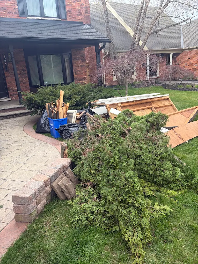 A front yard cleared of an old brush pile, scrap wood and a recycling bin outside a brick home