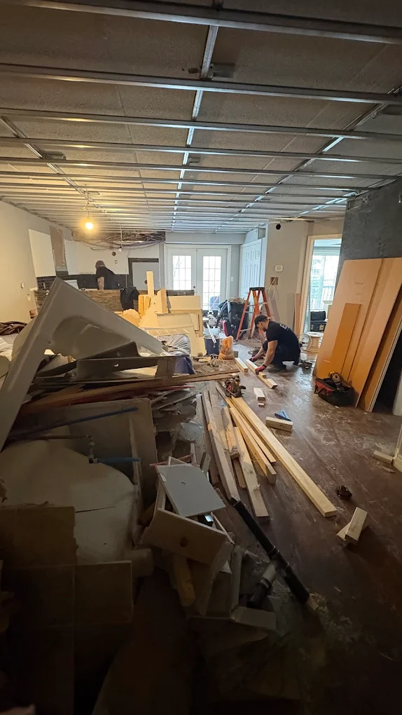 A crew member working through a gutted interior packed with renovation debris, lumber and torn-out drywall