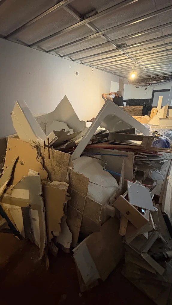 A large pile of torn-out drywall and demolition debris being cleared from a stripped interior
